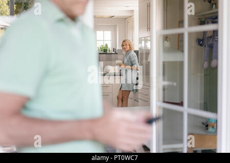 Reife Frau in der Küche zu Hause mit dem Menschen im Vordergrund. Stockfoto