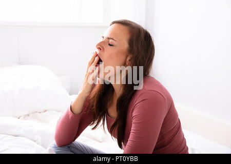 Schöne junge Frau Gähnen auf dem Bett im Schlafzimmer Stockfoto