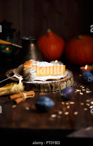 Stück pumpkin Cheesecake mit Puderzucker, Pflaumen, Kürbisse, Tischlampe auf einem dunklen Hintergrund Stockfoto