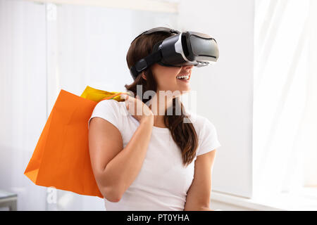 Lächelnde junge Frau mit Virtueller Realität Gerät für Shopping Erlebnis zu Hause Stockfoto