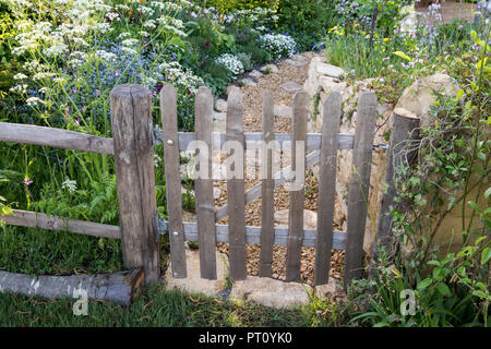 Rustikaler alter Parkettgarten Torzaun Wildblumen Blumen Landhaus Garten Pflanzung Kiesweg Cotswold Trockensteinwand Frühling UK Stockfoto