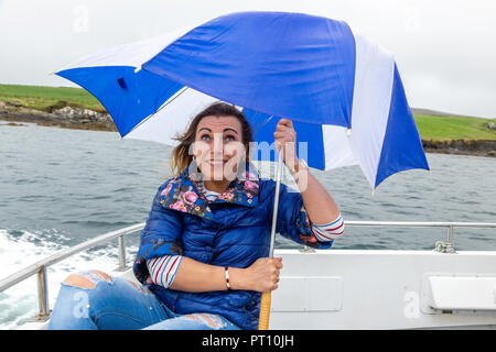 Blonde Frau auf einem Boot mit kaputten Regenschirm Stockfoto