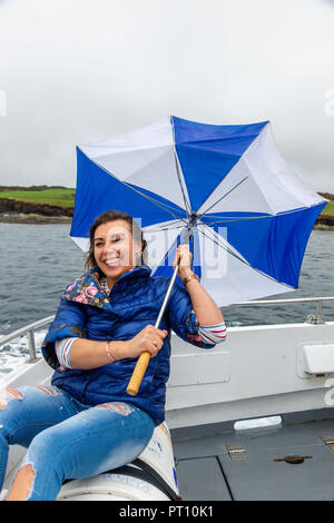 Blonde Frau auf einem Boot mit kaputten Regenschirm Stockfoto