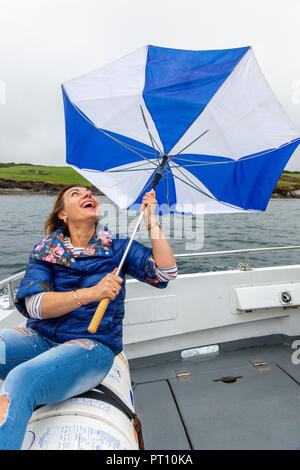 Blonde Frau auf einem Boot mit kaputten Regenschirm Stockfoto