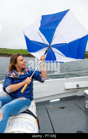 Blonde Frau auf einem Boot mit kaputten Regenschirm Stockfoto