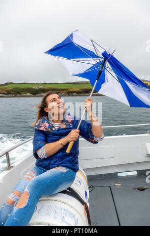 Blonde Frau auf einem Boot mit kaputten Regenschirm Stockfoto