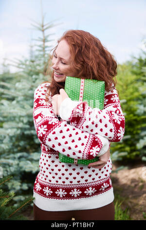 Happy rothaarige Junge Frau umarmt Weihnachtsgeschenk im Freien Stockfoto