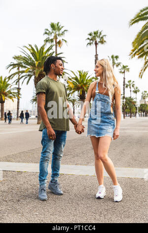 Spanien, Barcelona, multikulturelle junge Paar standing Hand in Hand an der Promenade Stockfoto