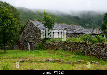 Traditionelle alte Schiefer und Stein 1-geschossige Scheune, mit Trockenmauern unter einem Senken bewölkter Himmel von Misty rain Stockfoto