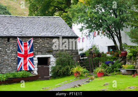 Gebäude in der kleinen Ortschaft Watendlath, Derwent, Cumbria, ein weiß gestrichene Teestube und Scheune in einen Union Jack Flagge drapiert. Stockfoto