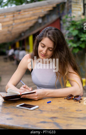 Junge Frau am Tisch sitzend Notizen Stockfoto