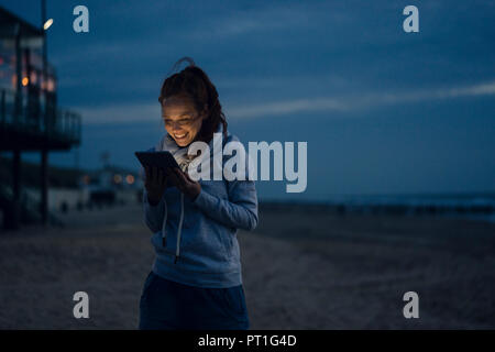Frau mit digitalen Tablette am Strand bei Sonnenuntergang Stockfoto