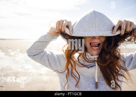 Frau Spaß zu haben an einem windigen Strand, mit Haube Stockfoto