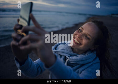 Frau mit Smartphone auf dem Strand bei Sonnenuntergang Stockfoto