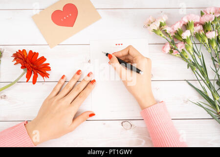 Frau schreibt Liebesbrief auf weißem Papier mit roten Herzen Form zahlen. Hand Postkarte für Saint Valentines Tag Feier gemacht. Schicken sie Briefe für Ihren lov Stockfoto