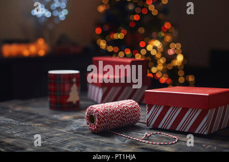 Rolle von rot-weißen packthread und geschenkboxen vor der beleuchteten Weihnachtsbaum Stockfoto