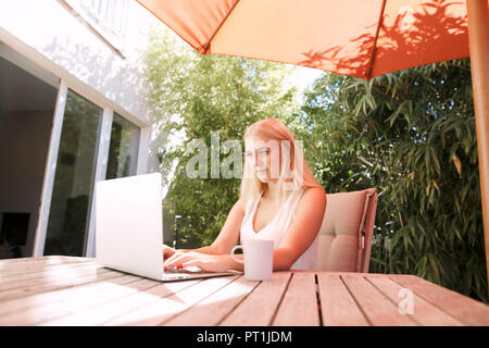 Junge Frau mit Laptop, sitzen auf den Gartentisch Stockfoto