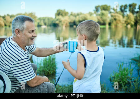 Großvater und Enkel zusammen Toasten am Seeufer Stockfoto