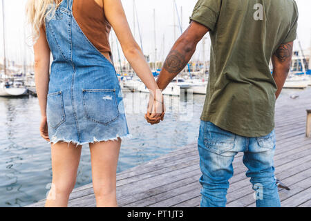 Rückansicht des multikulturellen junges Paar standing Hand in Hand auf der Jetty, Teilansicht Stockfoto