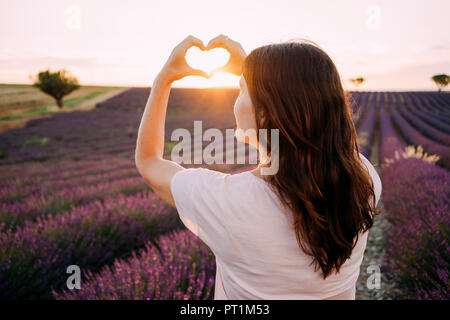 Frankreich, Valensole, zurück Blick auf Frau Gestaltung Herz mit ihren Händen vor lavendelfeld bei Sonnenuntergang Stockfoto