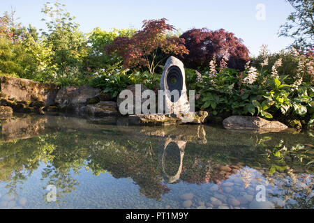 Japanischer Zen-Garten großes Teichwasser mit moosbedeckten Steinen mit Zantedeschia aethiopica - Rodgersia aesculifolia - Acer palmatum trees UK Stockfoto