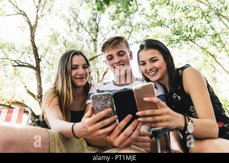 Drei glückliche Freunde auf der Suche nach Handys im Freien Stockfoto