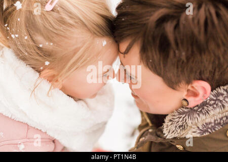 Kleines Mädchen kuschelte mit ihrer Mutter im Schnee Stockfoto