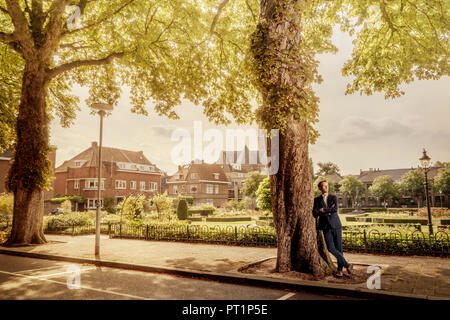 Niederlande, Venlo, Geschäftsmann, lehnte sich an einen Baum Stockfoto