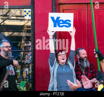 Holyrood Edinburgh, Edinburgh, Schottland, Vereinigtes Königreich, 6. Oktober 2018. Alle unter einem Banner (auob) schottischen März und Rally für Unabhängigkeit, mit Unterstützern auf der Royal Mile, dem Holyrood Park für eine Rallye. AOUB ist ein pro-unabhängigkeit Kampagne für deren Ziel ist es, in regelmäßigen Abständen zu März bis Schottland Unabhängigkeit erreicht. Eine lächelnde Frau hält stolz ein Ja Zeichen, da der märz Vergangenheit geht Stockfoto