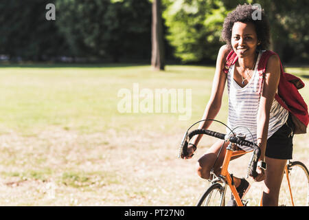 Portrait von lächelnden jungen Frau auf Fahrrad im Park Stockfoto