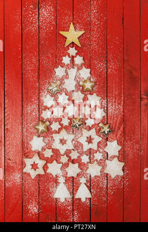 Weihnachtsplätzchen und sternförmige Christbaumkugeln bilden Weihnachtsbaum auf rot Holz- Hintergrund Stockfoto