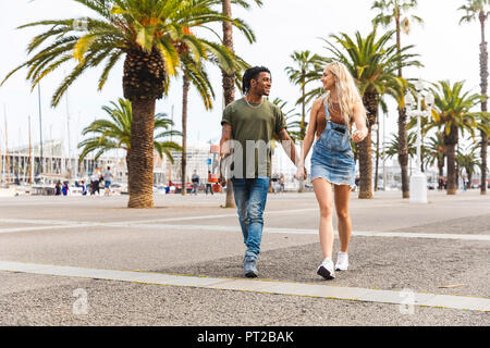 Spanien, Barcelona, multikulturelle junge Paar Hand in Hand an der Promenade Stockfoto