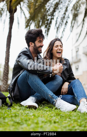 Spanien, Barcelona, Lachen junges Paar sitzt auf Wiese Stockfoto