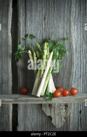 Bündel von grünem und weißem Spargel, Tomaten, Petersilie und Pfeffer vermischt auf Holz Stockfoto