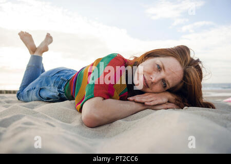 Rothaarige Frau in Sand am Strand liegen Stockfoto