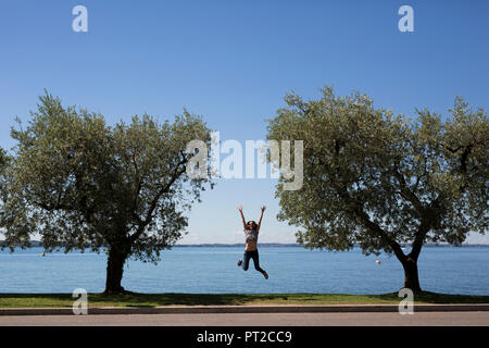 Italien, Gardasee, glückliche junge Frau, springen in die Luft zwischen zwei Bäumen Stockfoto