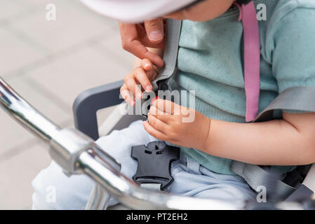 Mutter und Tochter, die Tochter sitzt im Kindersitz und Befestigung des Sicherheitsgurts Stockfoto