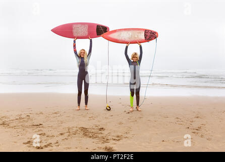 Spanien, Madrid, zwei junge Surfer am Strand halten ihre Surfbretter Stockfoto