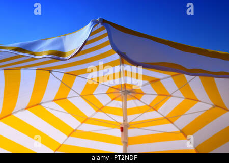 Big weiß und gelb gestreifte Schirm und klaren Sommer Himmel, gelb-weiß gestreifte Sonnenschirm vor dem azurblauen Himmel als Symbol für Ferienhäuser Stockfoto