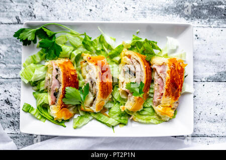 Swiss roll, Blätterteig mit Wurst, Fleisch, Käse, Zwiebel, Petersilie und Salat auf Teller Stockfoto