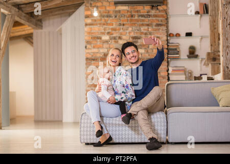 Glückliche junge Eltern eine selfie auf der Couch zu Hause mit Ihrem Baby girl Stockfoto