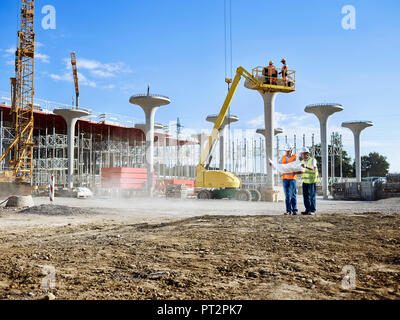 Die Arbeiter auf der Baustelle bei Blueprint mit dem Architekten suchen Stockfoto