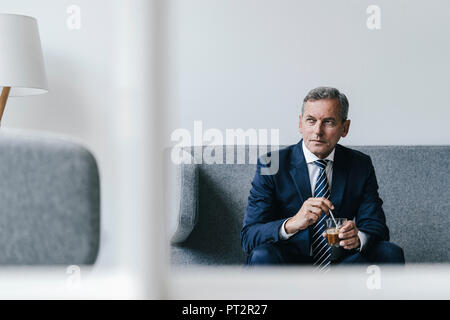 Reifen Geschäftsmann mit einem Glas Kaffee sitzen auf der Couch in seinem Büro Stockfoto