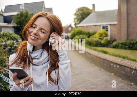 Rothaarige Frau mit Kopfhörer und Smartphone in der Stadt Stockfoto