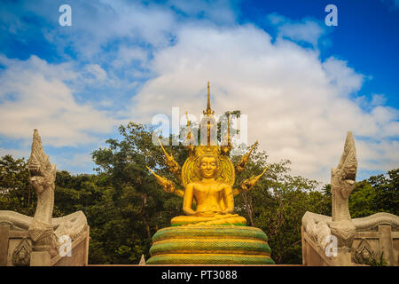 Wunderschöne goldene Buddha Statue mit sieben Phaya Naga Köpfe unter weißen Wolken und blauer Himmel. Outdoor golden sitzender Buddha Bild geschützt durch Stockfoto