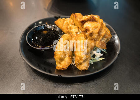 Eine schwarze Platte der japanischen Gyoza-teigtaschen sitzen auf einem rustikalen schwarz Tisch. Stockfoto