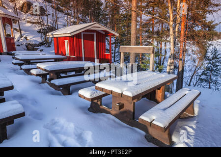 Ländliche Winterlandschaft mit generischen Red Cottage aus Holz und Gartenmöbeln unter Schnee, Finnland Stockfoto