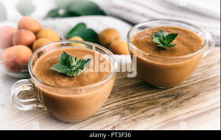 Zwei Tassen Aprikose Smoothie mit Minze Blütenblättern dekoriert. Es gibt ganze Aprikosen in der Nähe. Stockfoto