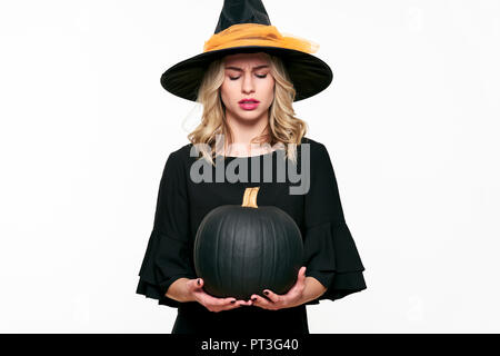 Wütend Halloween Hexe mit großen schwarzen Kürbis, auf. Schöne junge Frau in Hexen Hut und Kostüm holding Kürbis über weiß Bac Stockfoto