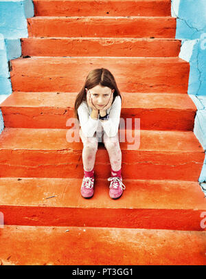 Unzufrieden 8 jähriges Mädchen sitzen auf orange Schritte. Stockfoto